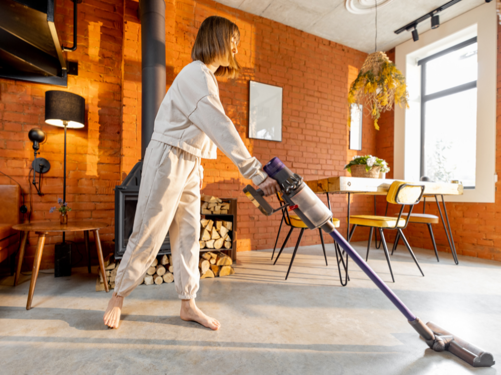 Vrouw in joggingspak stofzuigt huis met steelstofzuiger.